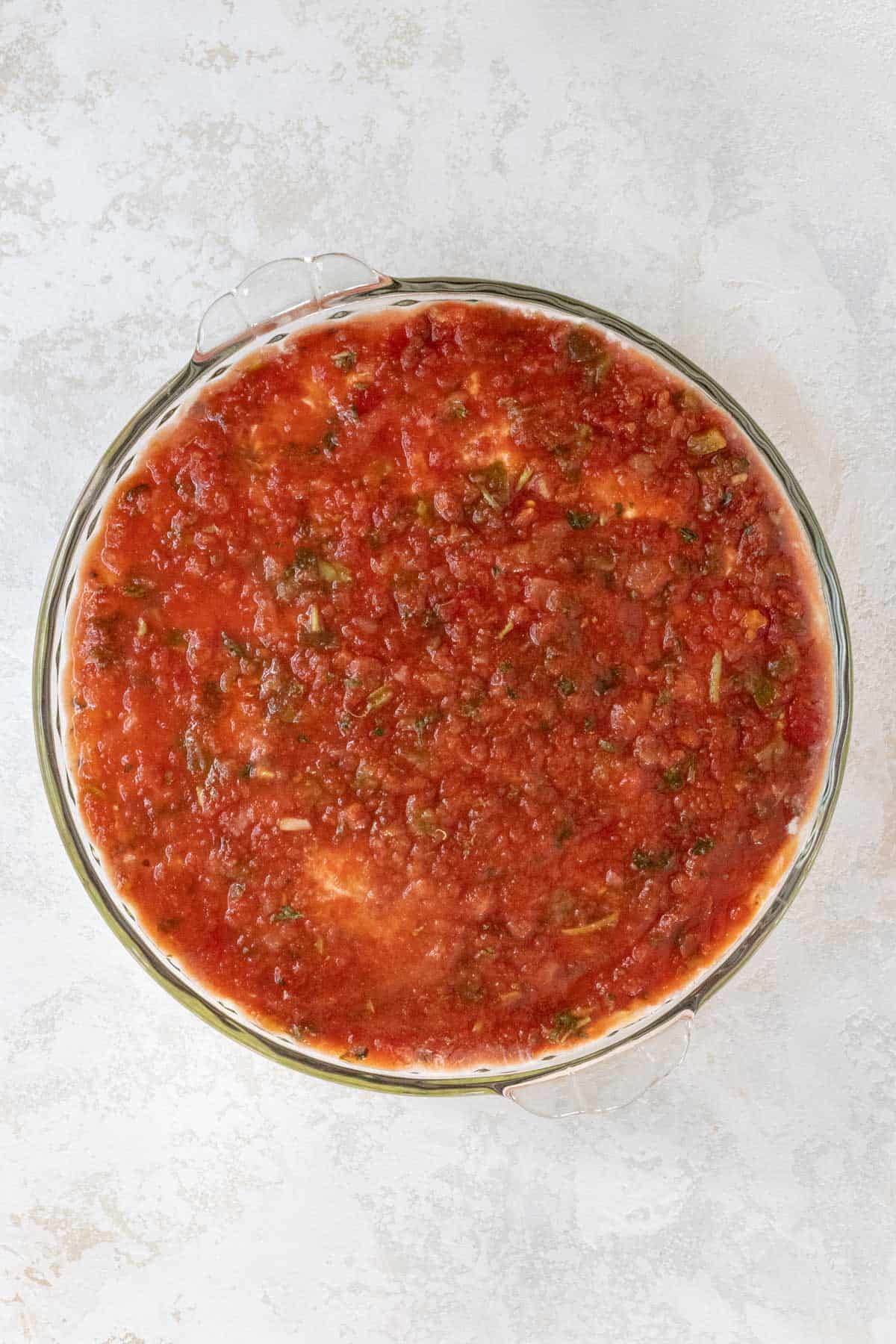 Salsa spread out over the seasoned sour cream in a large pie dish.