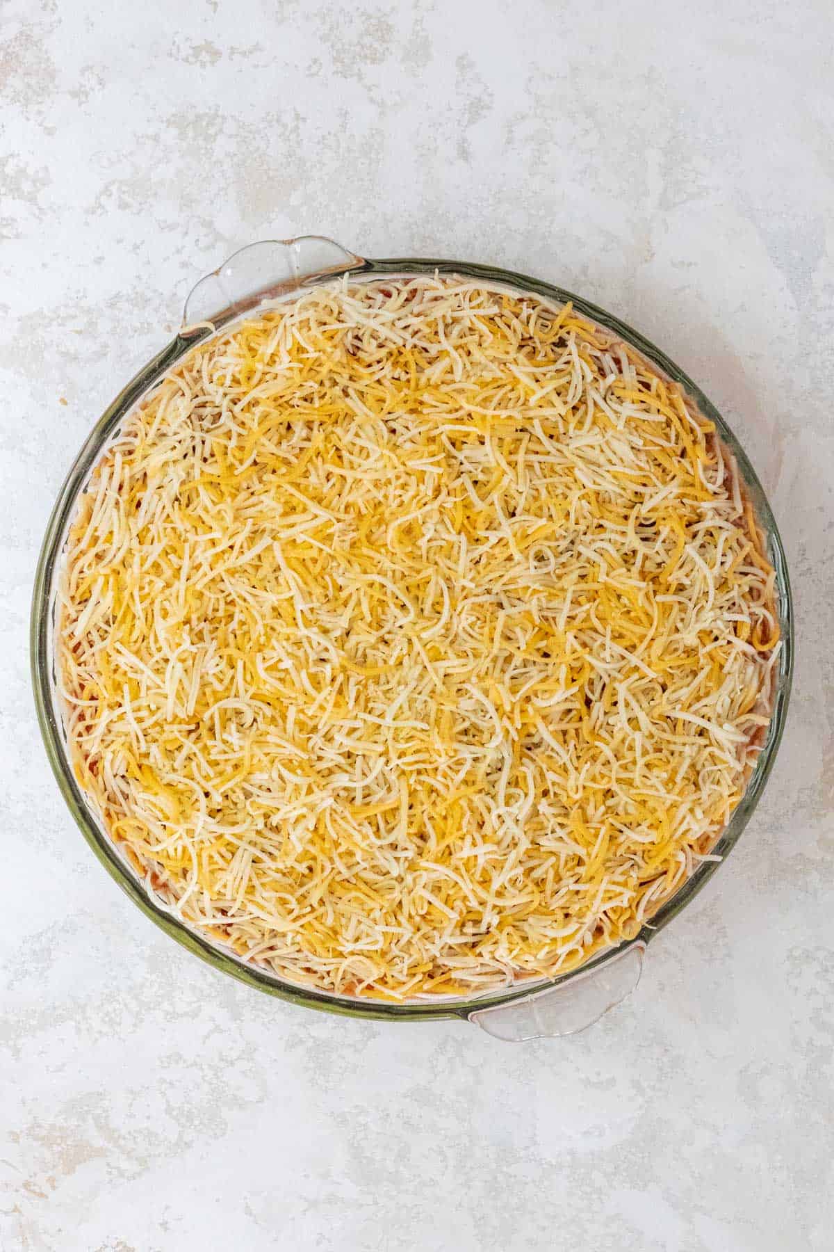 Shredded Mexican cheese sprinkled over the salsa in a large pie dish.