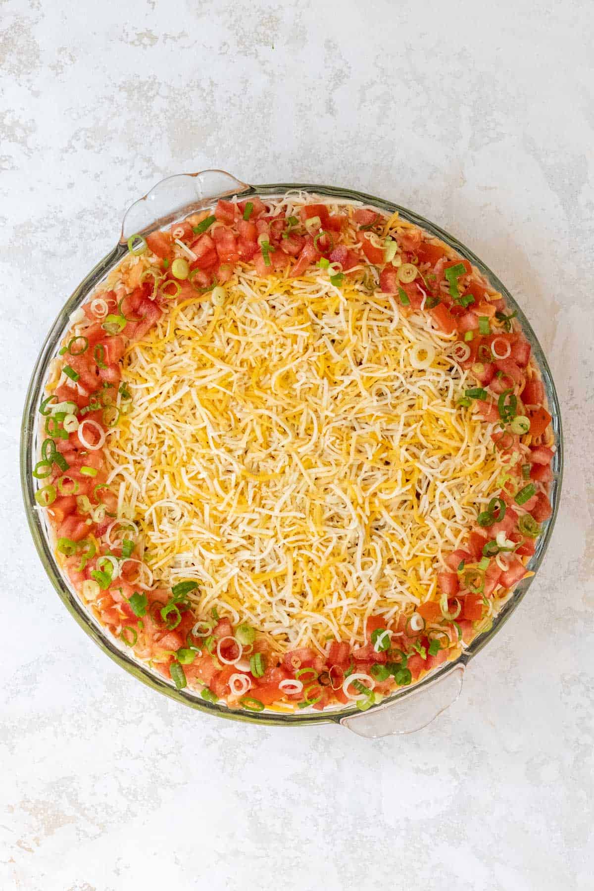 Chopped tomatoes and scallions on top of the shredded cheese and around the perimeter of a large pie dish.