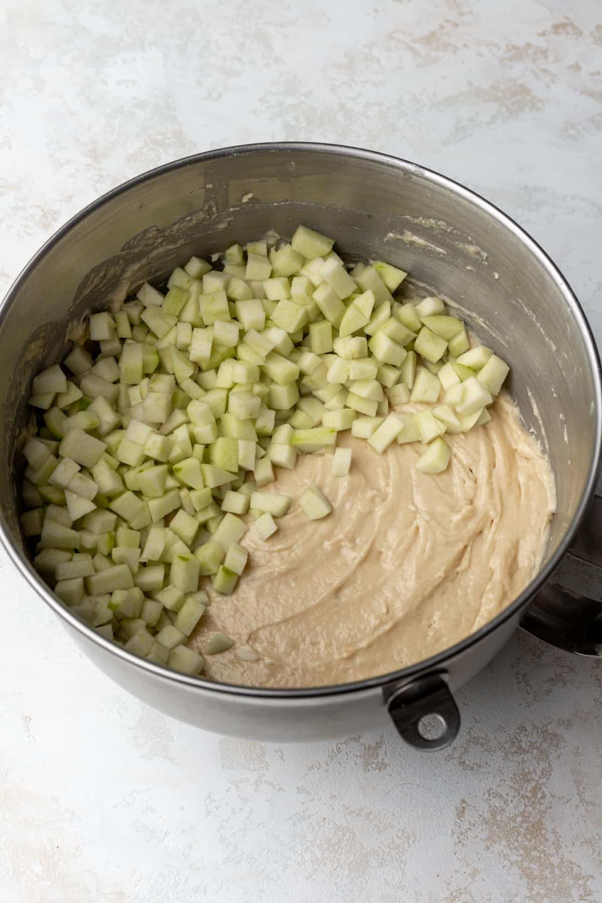 Raw apple cider cake batter with diced apples on top in a large mixing bowl.