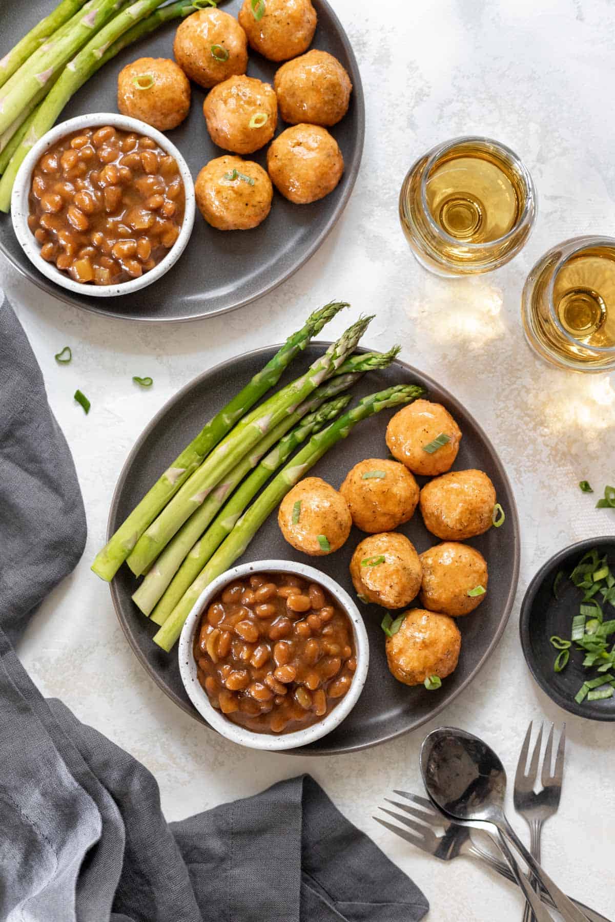 2 plates filled with honey bourbon salmon meatballs, asparagus, and baked beans.