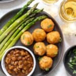 Honey bourbon glazed salmon meatballs on a gray plate with a side of asparagus and baked beans.