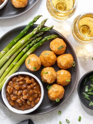 Honey bourbon glazed salmon meatballs on a gray plate with a side of asparagus and baked beans.