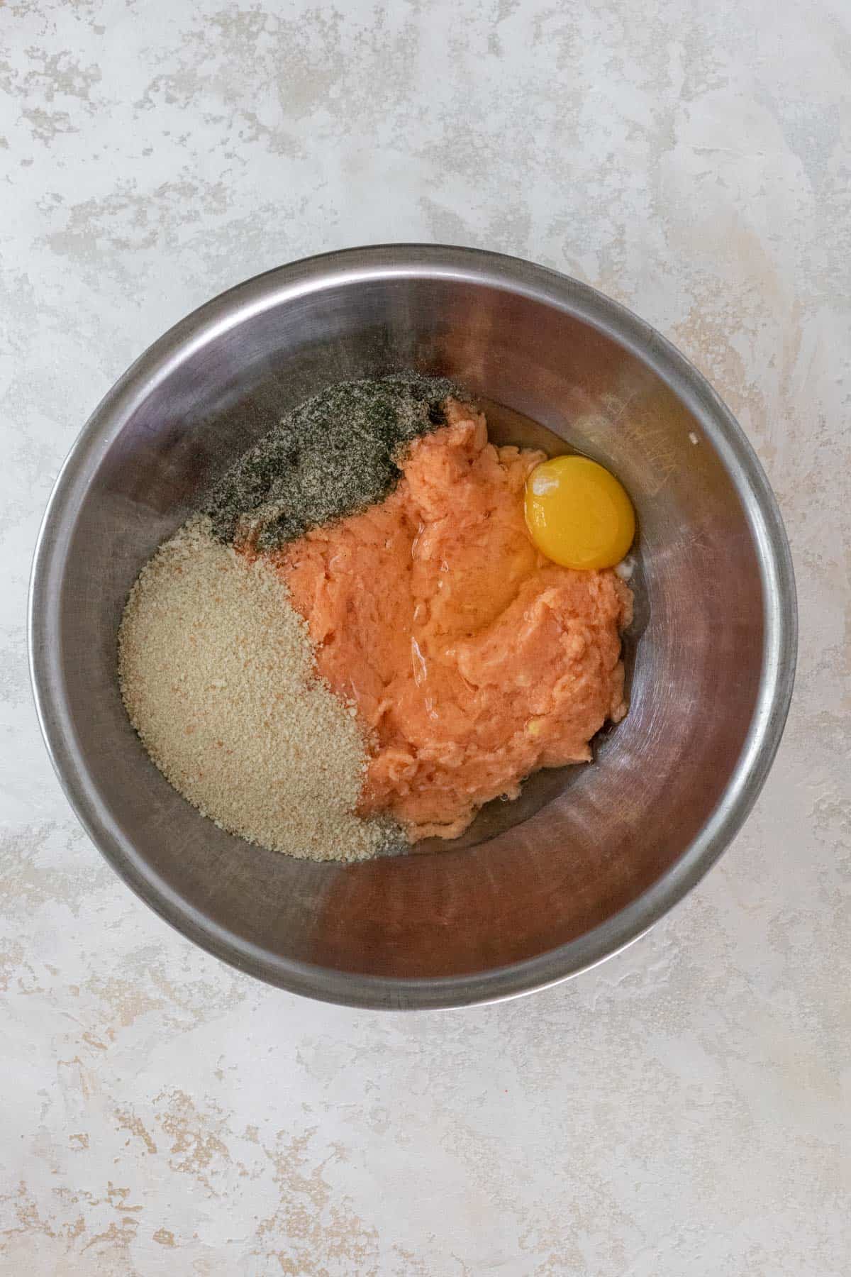 "Ground salmon", egg, breadcrumbs, and seasonings in a metal mixing bowl.