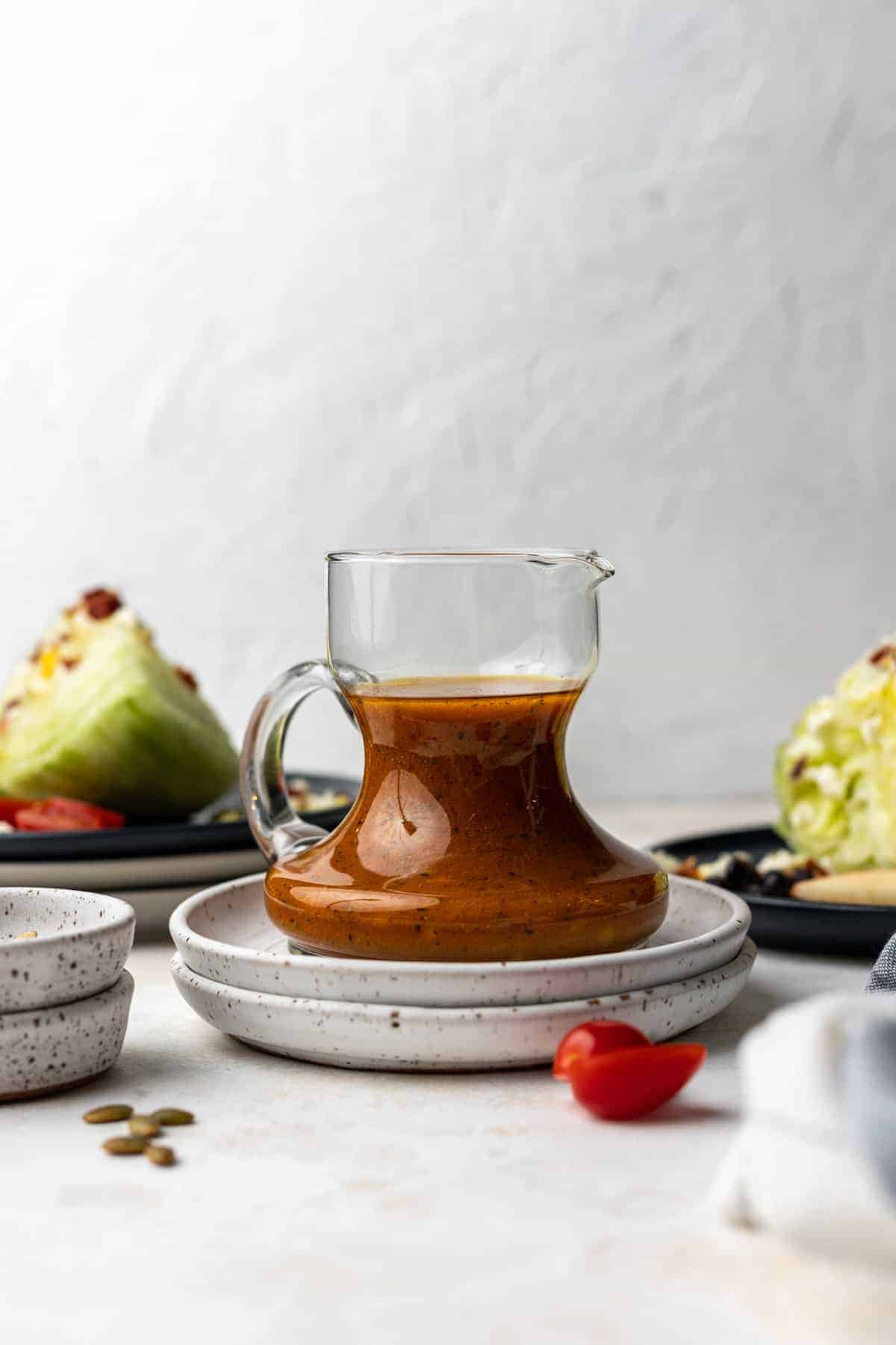 Pumpkin salad dressing in a small glass pitcher with wedges of salad and salad toppings next to it.