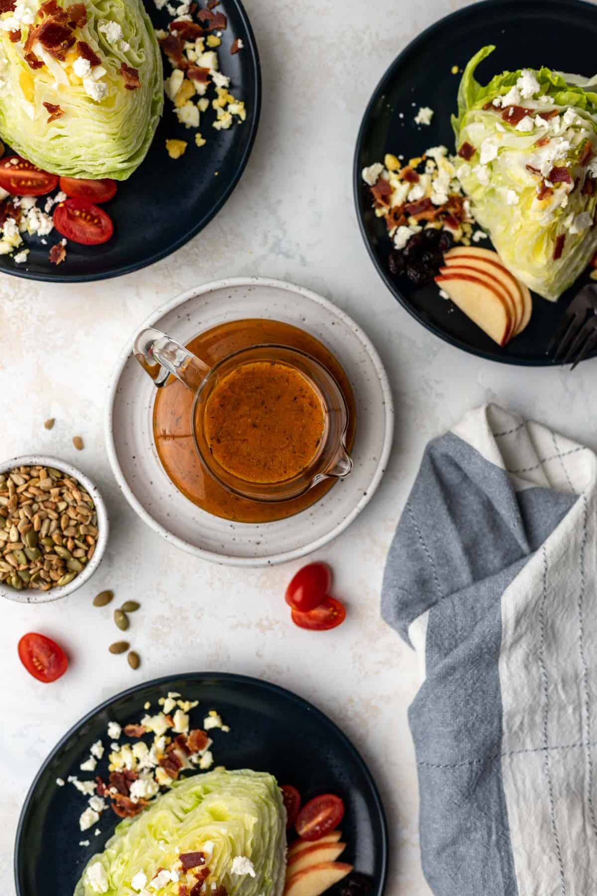 An overhead view of fall pumpkin dressing in a glass pitcher and 3 salads surrounding it.