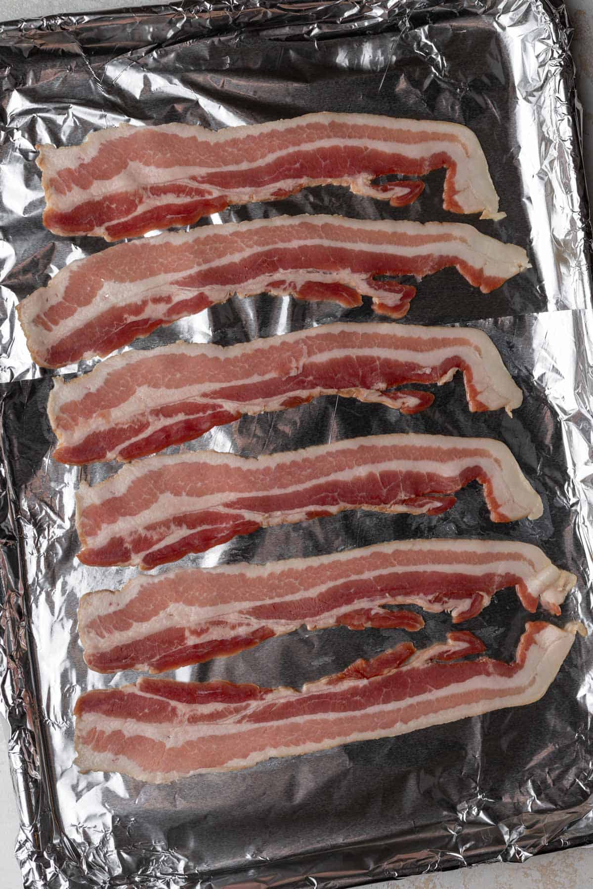 Bacon lined up on a sheet pan covered in foil.