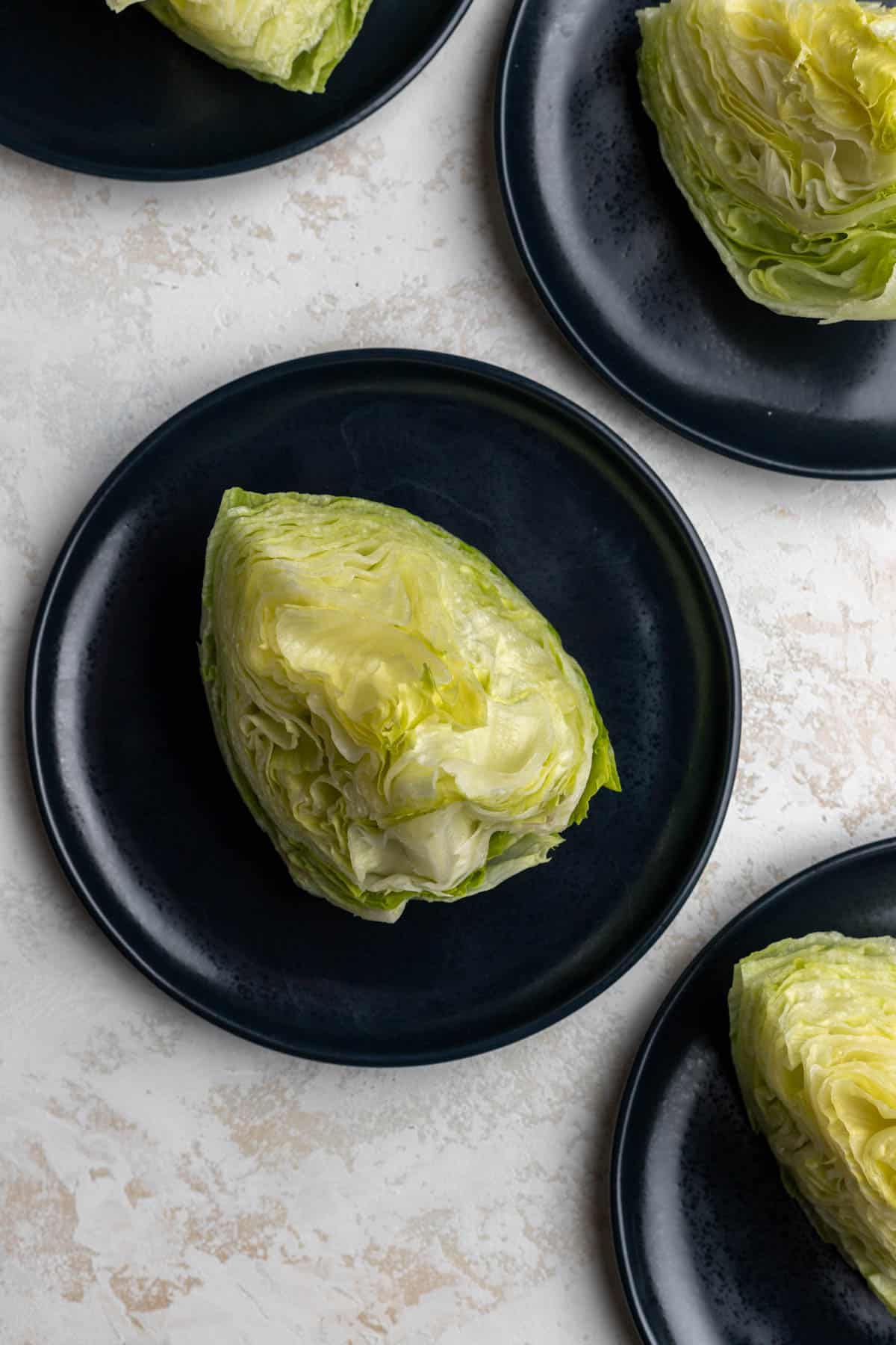 Wedges of iceberg lettuce on 4 blue plates.