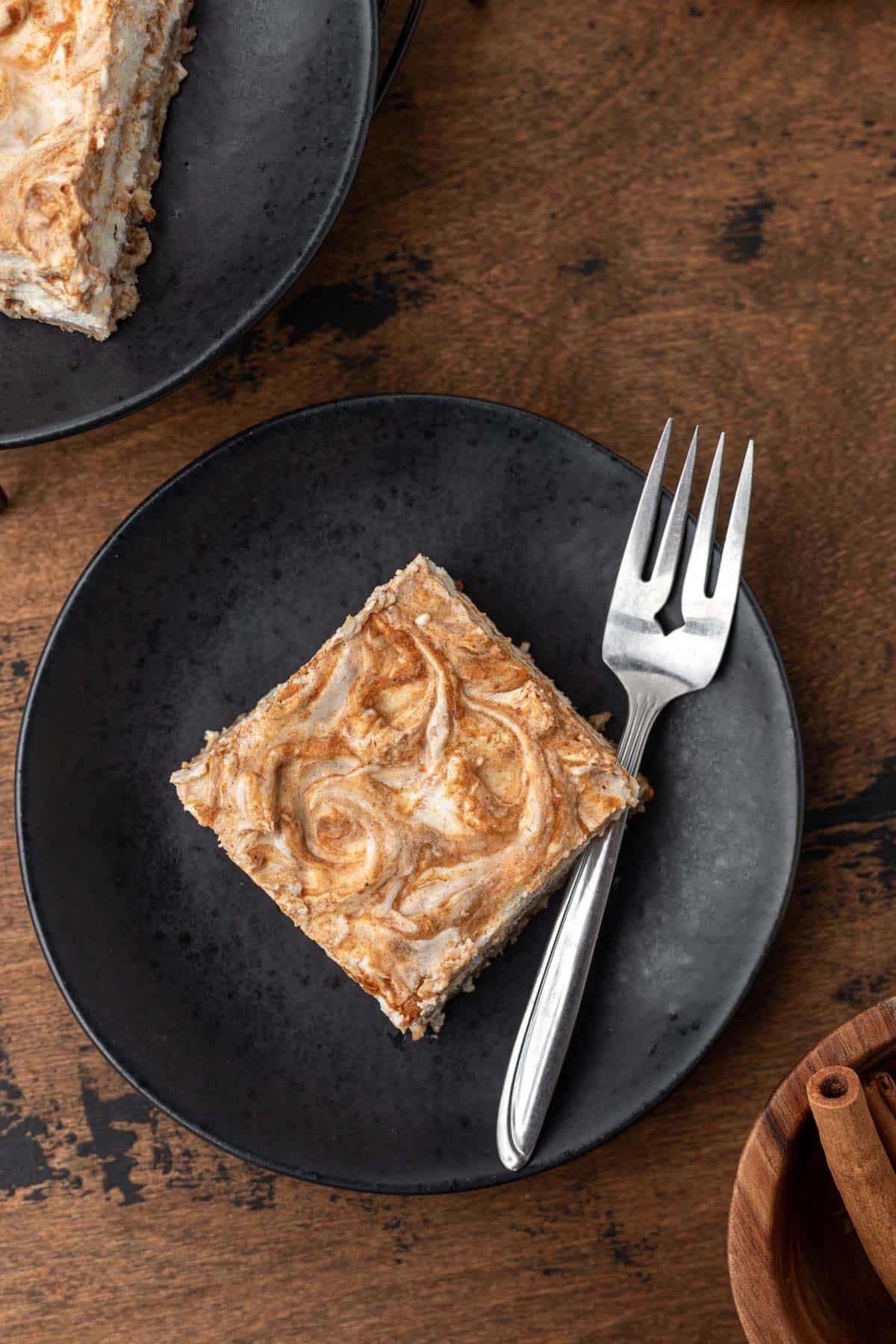 A pumpkin swirl cheesecake bar on a black plate with a fork to the side.