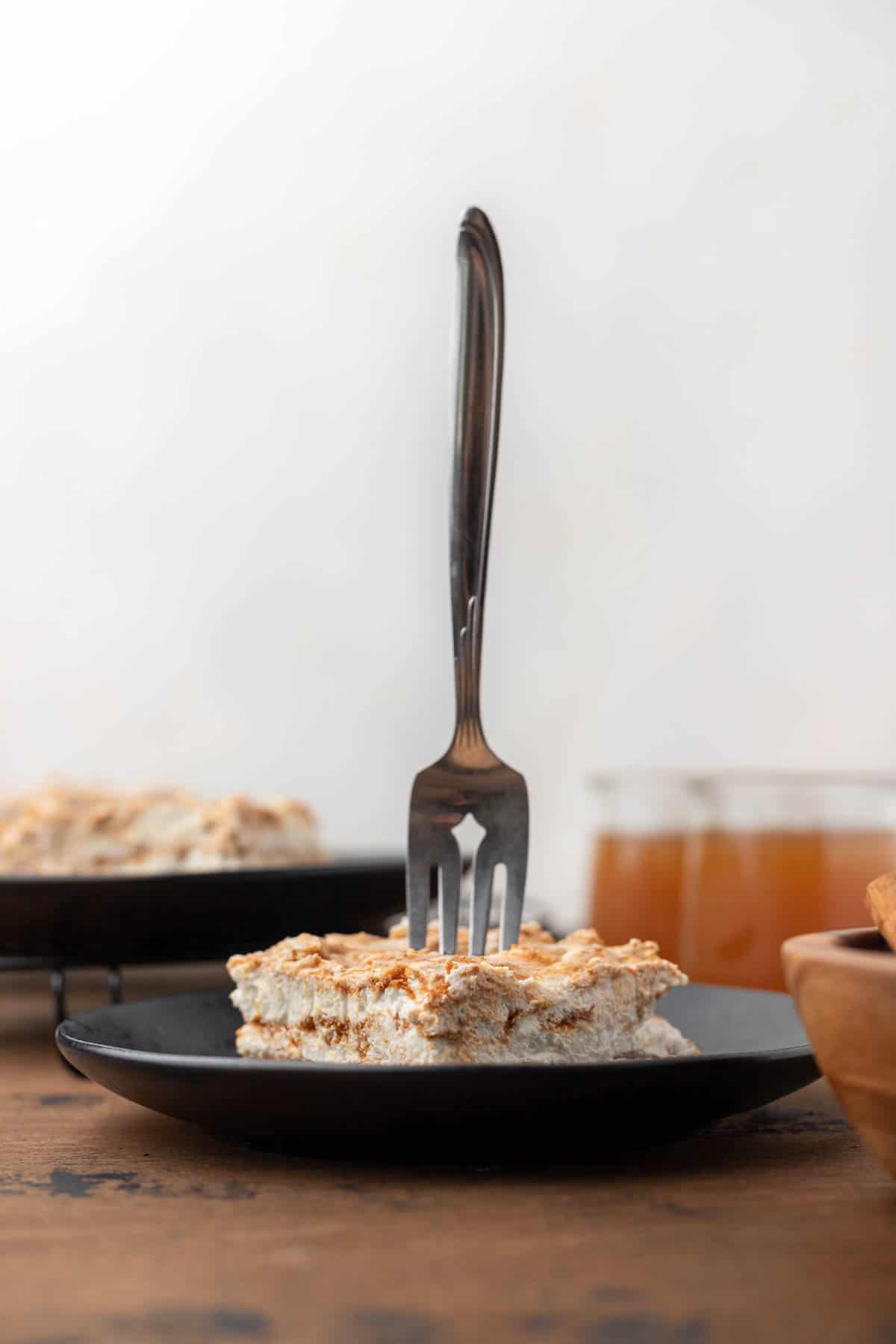 A fork sticking out of a healthy pumpkin swirl cheesecake bar with cups of apple cider next to it.