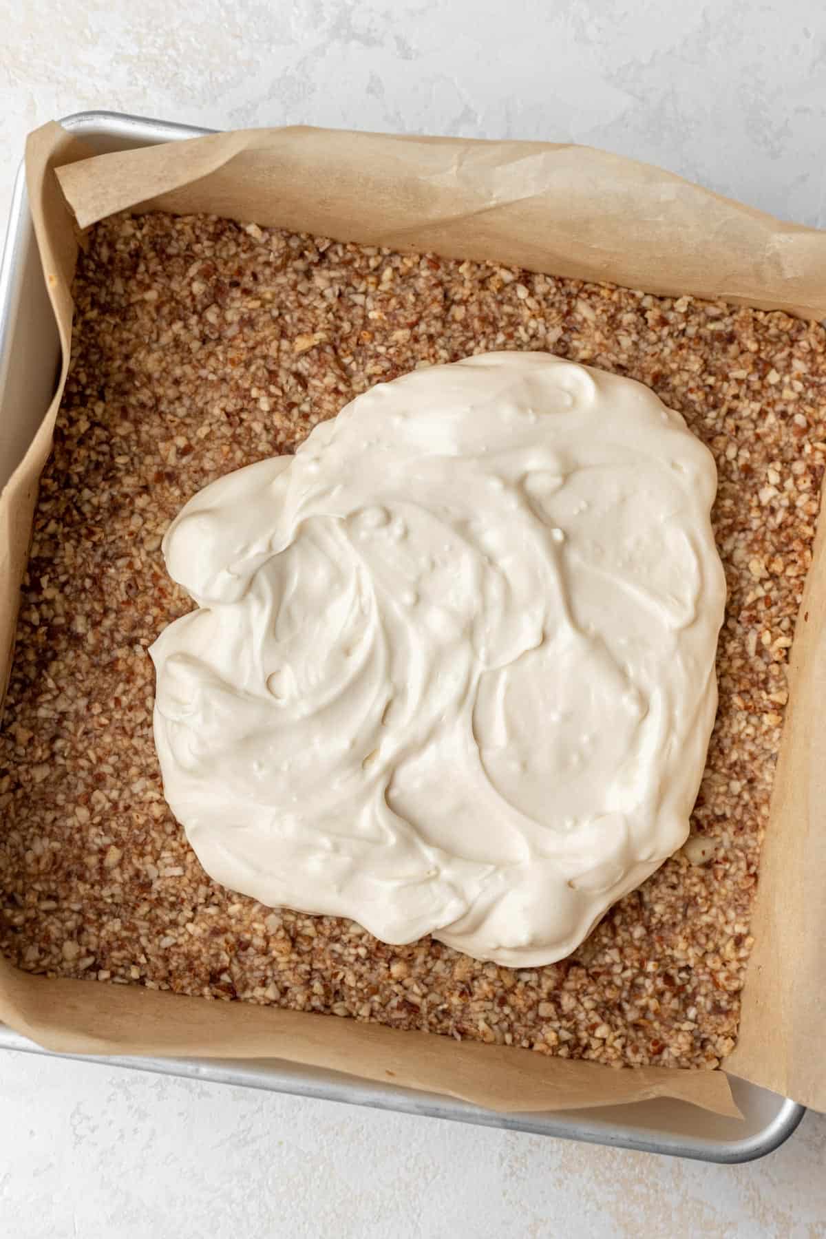 Cheesecake batter poured on top of almond crust in a cake pan.