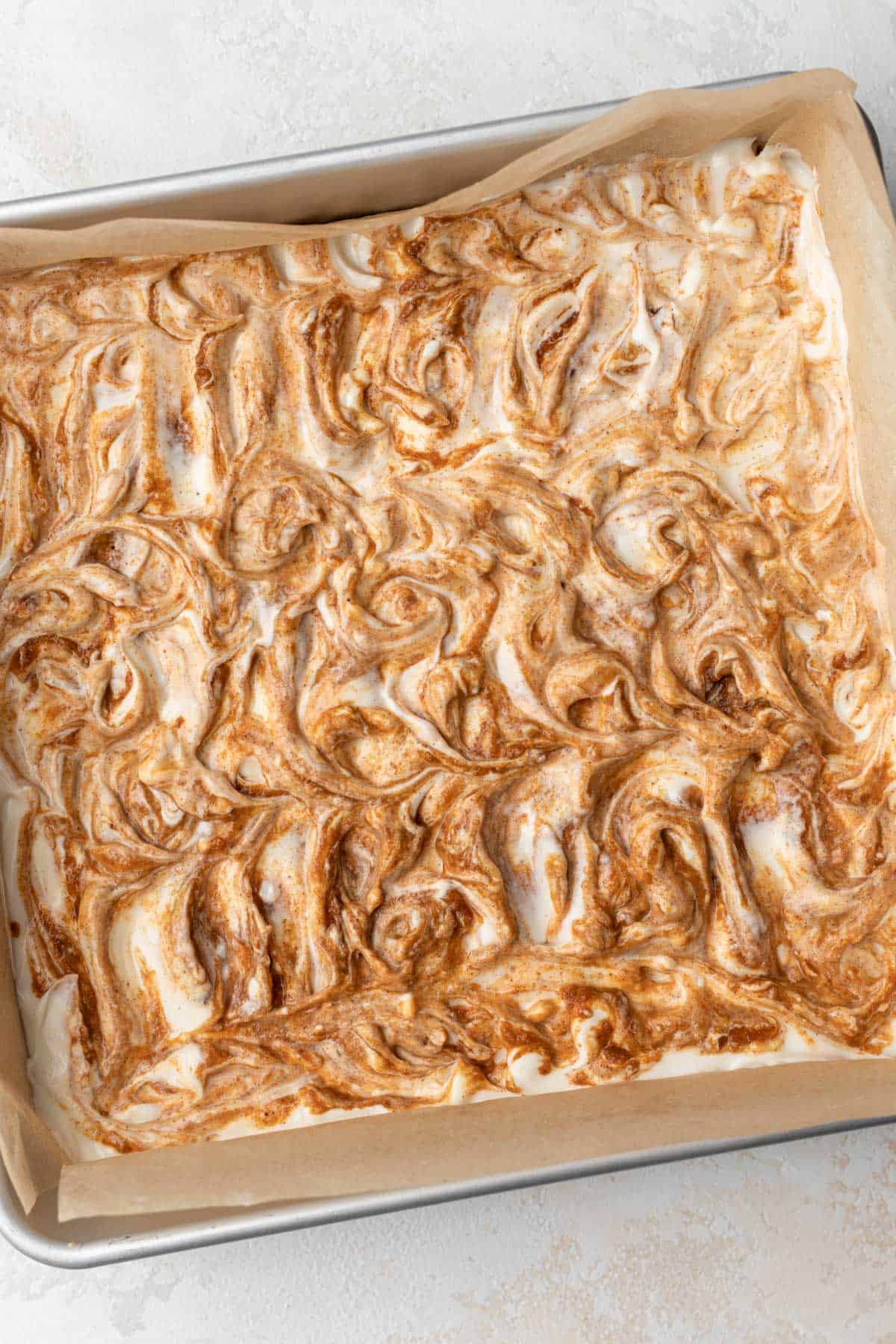 Spiced pumpkin puree swirled into the plain cheesecake batter in a cake pan.