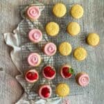 Almond cupcakes on a cooling rack with a swirl of strawberry buttercream.