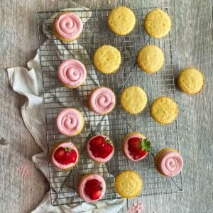 Almond cupcakes on a cooling rack with a swirl of strawberry buttercream.