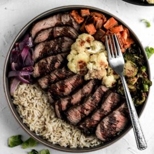 Balsamic steak in a bowl with brown rice, sweet poatoes, cauliflower, and brussels sprouts.