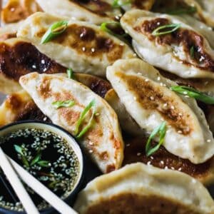 Chicken dumplings on a serving tray with sesame soy dipping sauce.