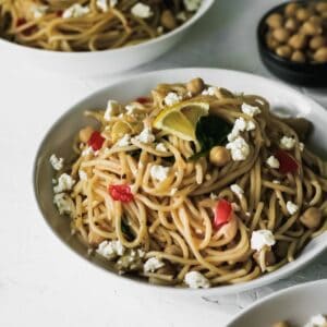 Garlic olive oil pasta in a bowl topped with feta and fresh vegetables.