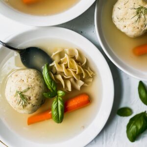 Matzo ball soup in white bowls with noodles and carrots.