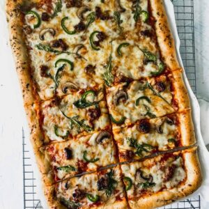 Mushroom, sausage, and arugula pizza on a cooling rack.