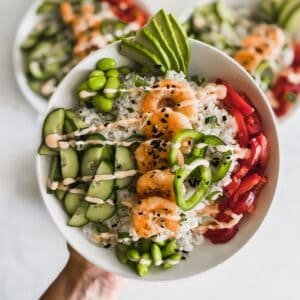 Shrimp on top of sushi rice with cucumbers, edamame, avocado, and peppers.