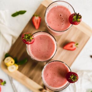 Strawberry banana smoothie in 3 cups with a garnish of fresh strawberries.