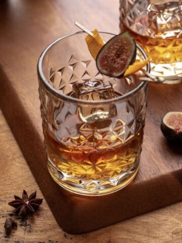 A vanilla fig old fashioned garnished with an orange peel and fresh fig.