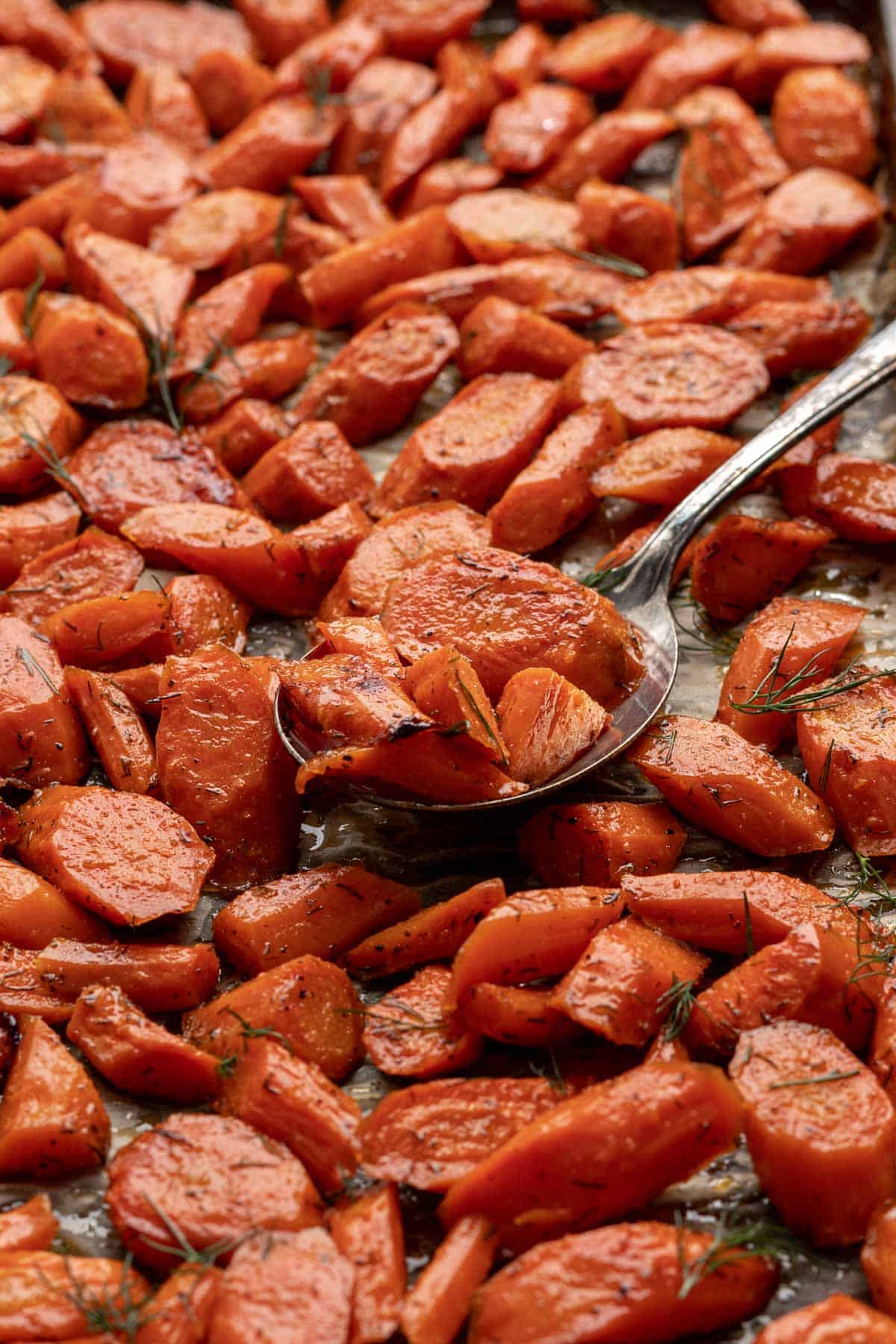 Roasted brown sugar and dill carrots on a sheet pan with a serving spoon scooping them up.