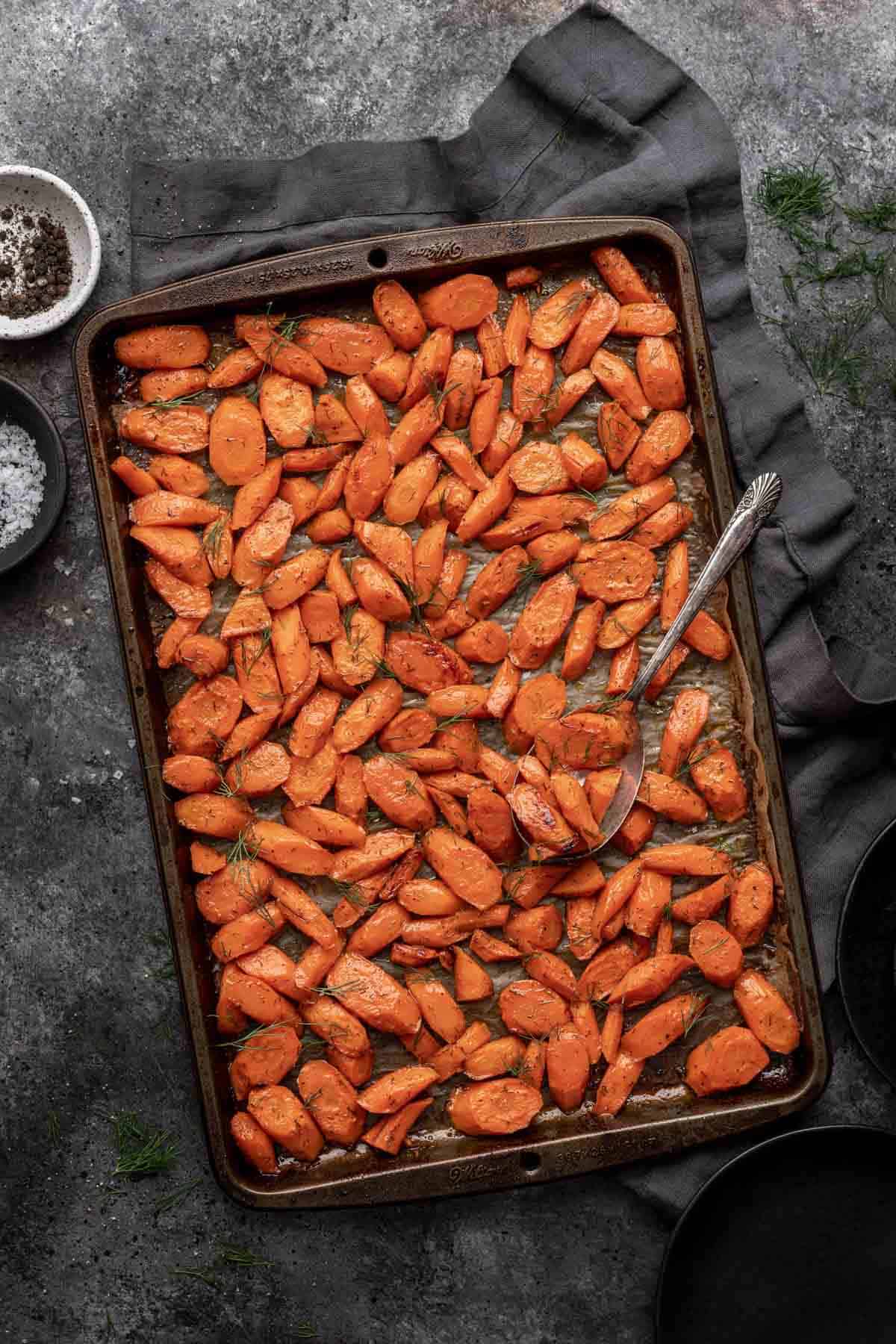 Brown sugar and dill roasted carrots on a sheet pan with a serving spoon.