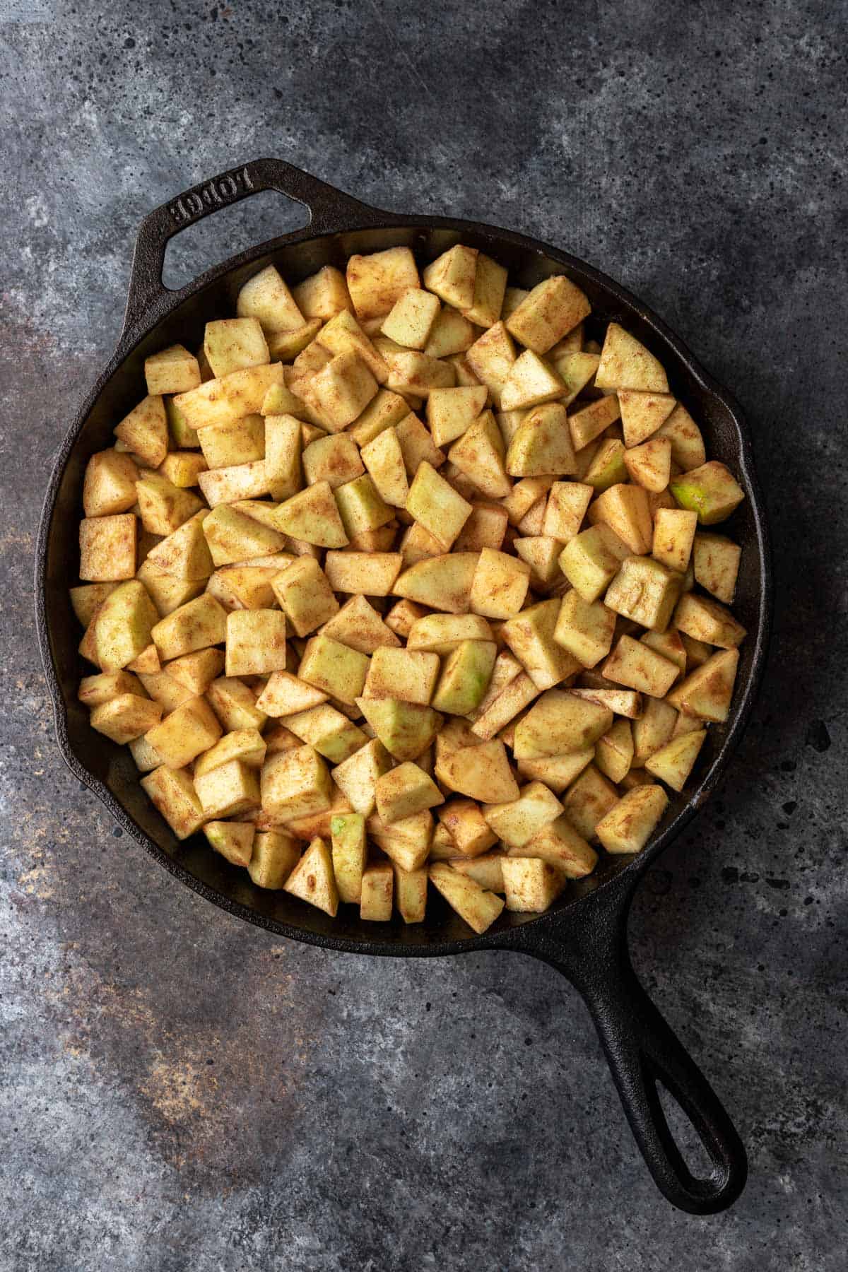 Diced apples mixed with caramel sauce in prepared cast iron skillet.