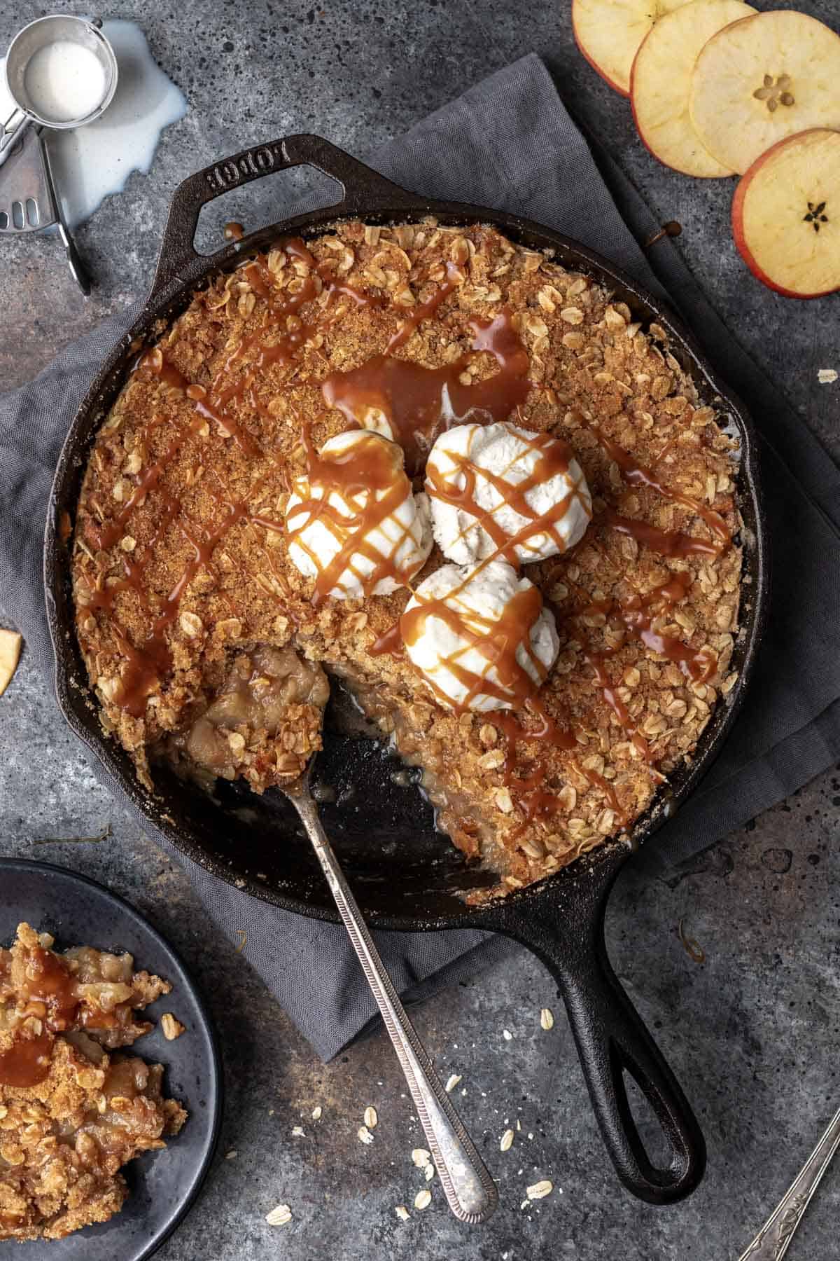 Bourbon apple crisp in a cast iron skillet with vanilla ice cream and a drizzle of caramel.