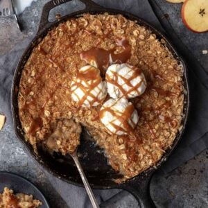 Bourbon apple crisp in a cast iron skillet with vanilla ice cream and a drizzle of caramel.