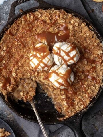 Bourbon apple crisp in a cast iron skillet with vanilla ice cream and a drizzle of caramel.