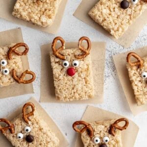 Reindeer rice krispie treats arranged on parchment paper with pretzel antlers, candy eyes, and a red candy nose.