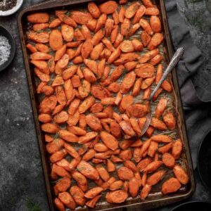 Brown sugar and dill roasted carrots on a sheet pan with a serving spoon.