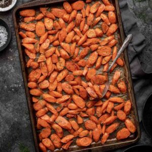 Brown sugar and dill roasted carrots on a sheet pan with a serving spoon.