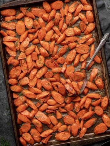 Brown sugar and dill roasted carrots on a sheet pan with a serving spoon.