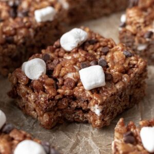 A hot chocolate rice krispie treat topped with mini marshmallows and chocolate chips with a bite taken out.