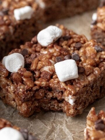 A hot chocolate rice krispie treat topped with mini marshmallows and chocolate chips with a bite taken out.