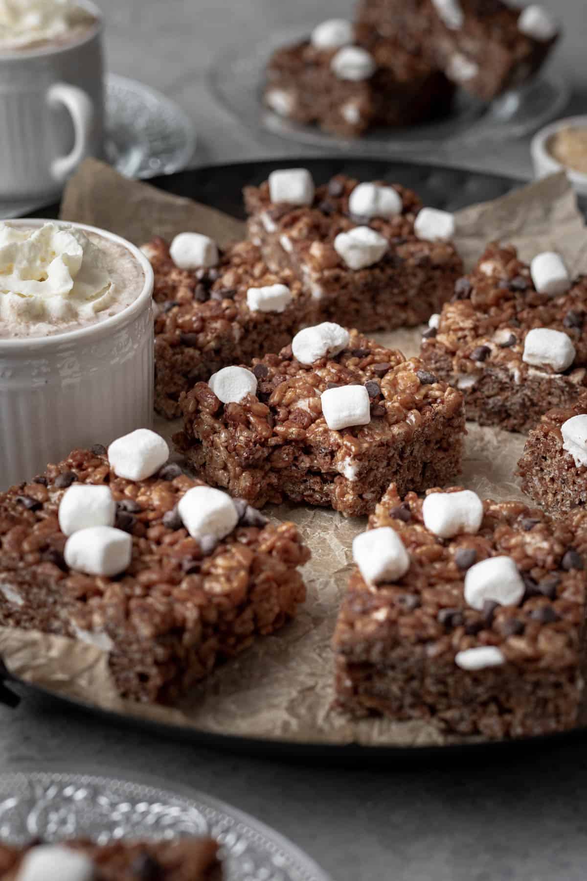 A hot chocolate rice krispie treat topped with mini marshmallows and chocolate chips with a bite taken out.