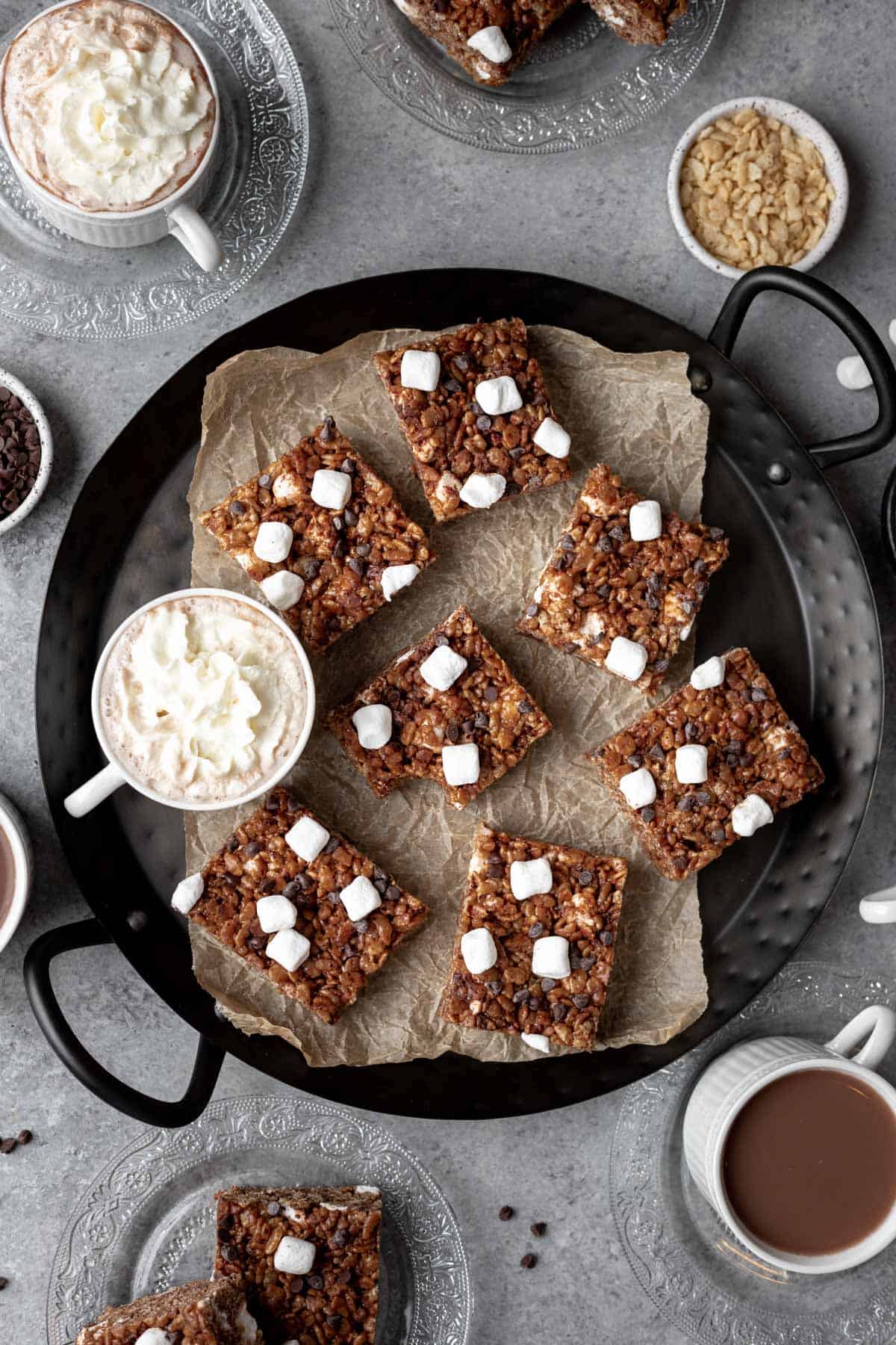 Hot chocolate rice krispie treats on a serving tray with cups of hot cocoa.