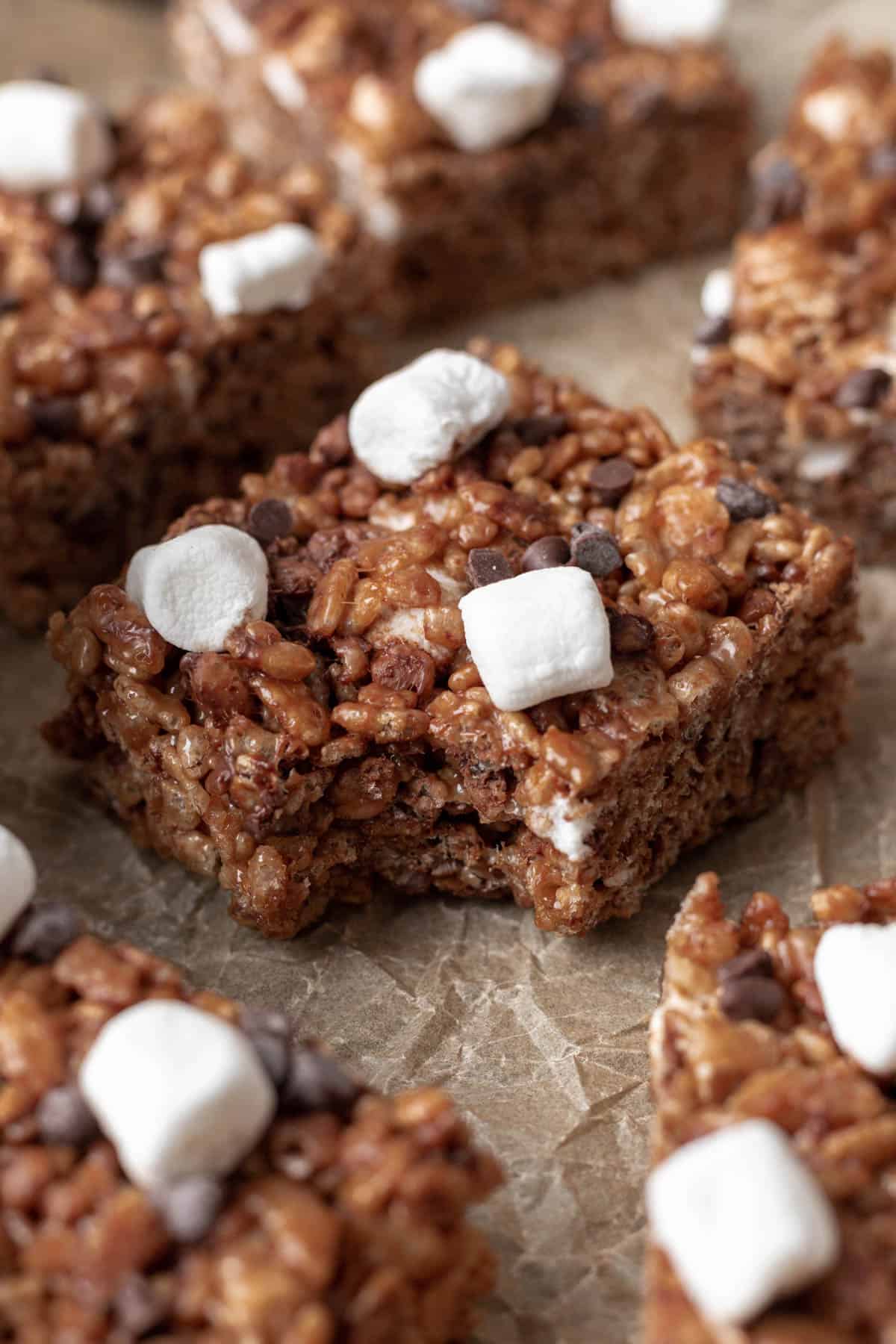 A cocoa rice krispie treat topped with marshmallows and chocolate chips with a bite taken out.
