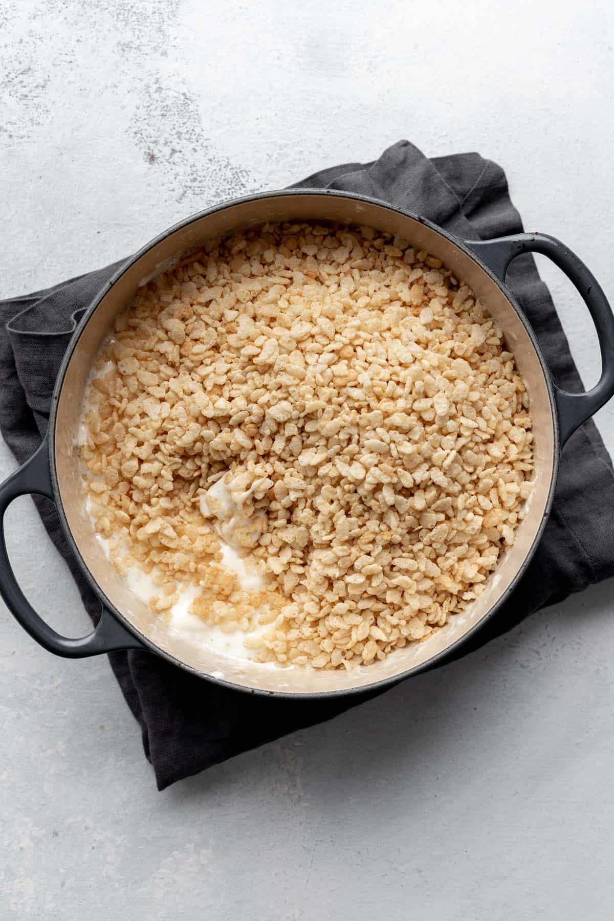 Rice cereal on top of melted marshmallows in a large pot.