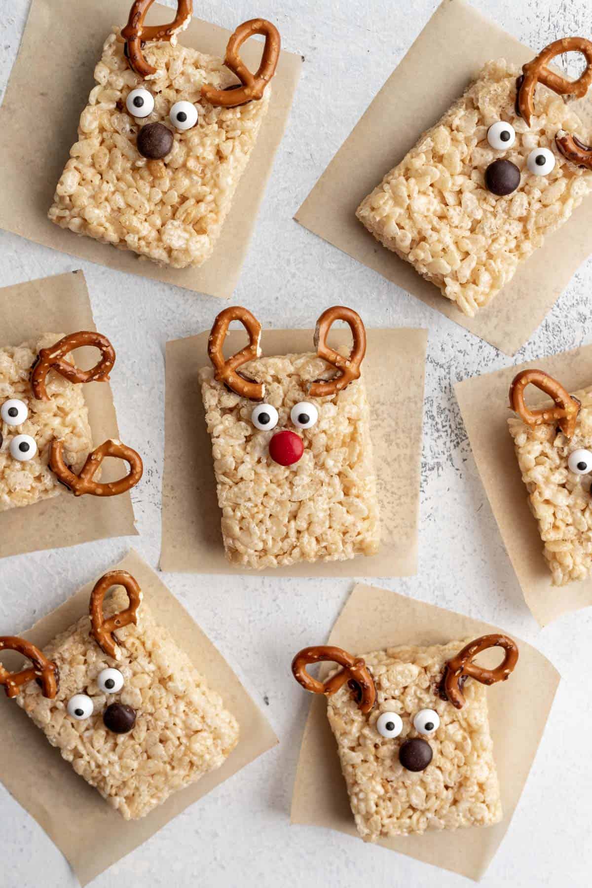 Reindeer rice krispie treats arranged on parchment paper with pretzel antlers, candy eyes, and a red or brown candy nose.
