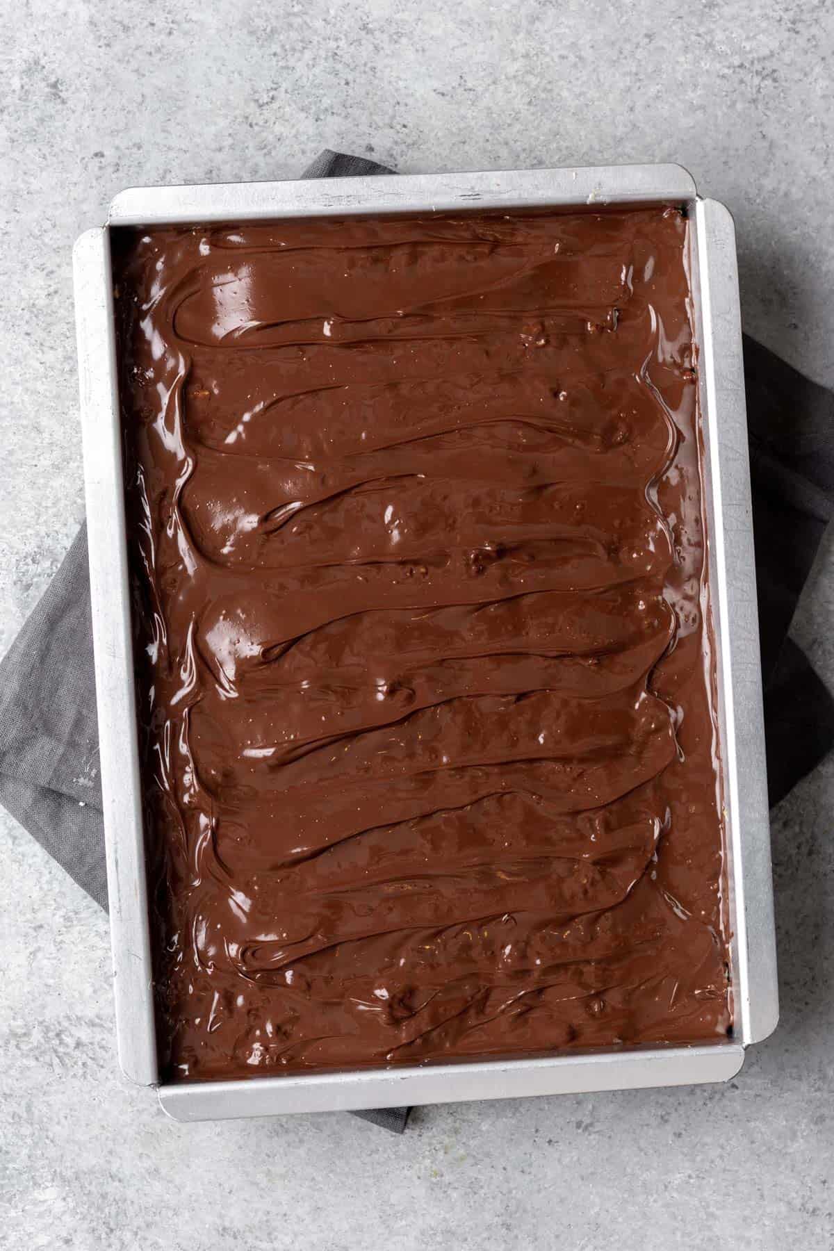 Melted chocolate spread over smores rice krispie treats in a 9x13 baking pan.