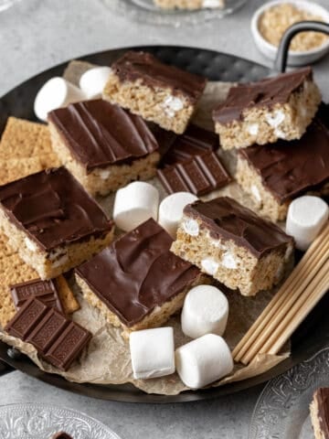 Smores rice krispie treats on a serving platter with big marshmallows, hersheys chocolate, and graham crackers.