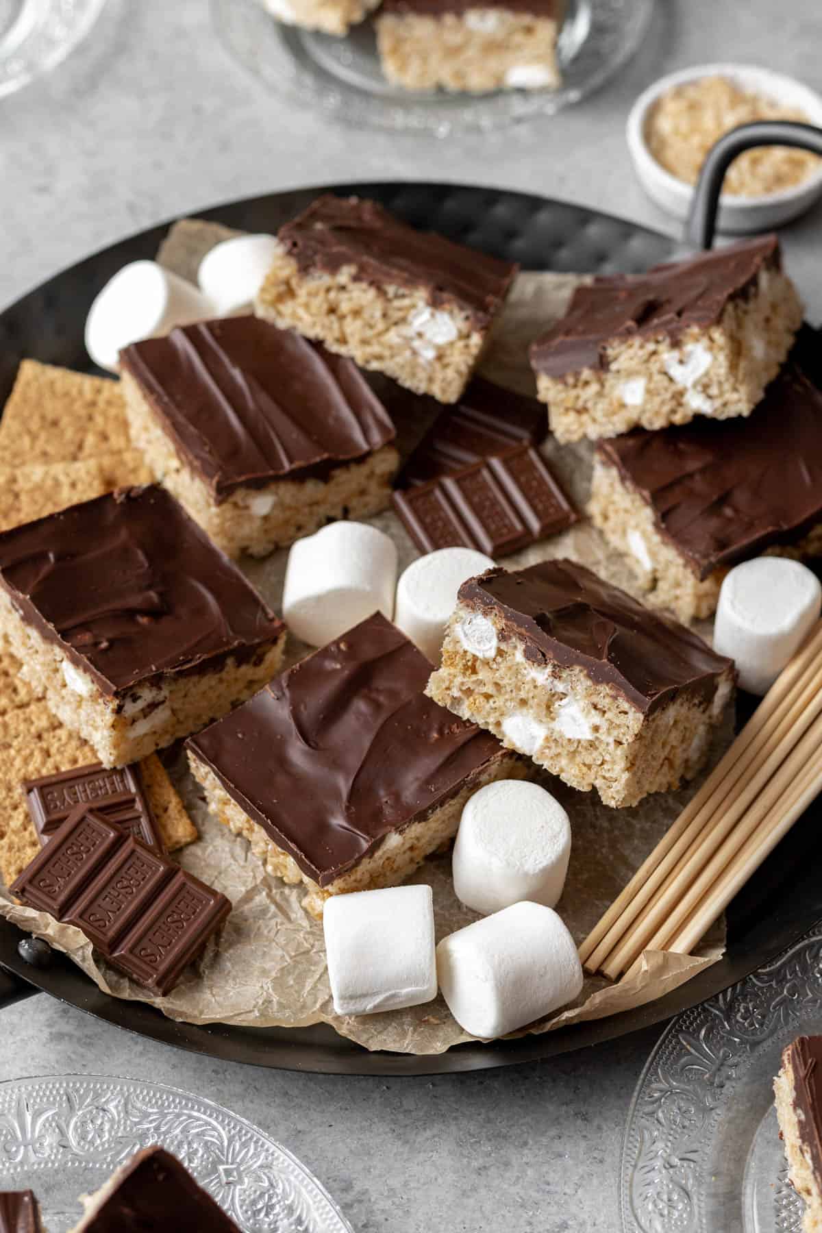 Smores rice krispie treats on a serving platter with big marshmallows, hersheys chocolate, and graham crackers.