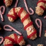 Peppermint candy cane rice krispie treats on a dark gray backdrop with small candy canes around it.