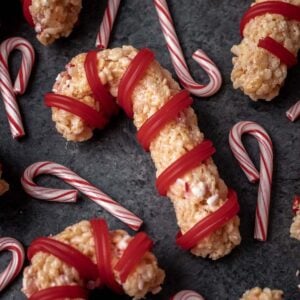 Peppermint candy cane rice krispie treats on a dark gray backdrop with small candy canes around it.