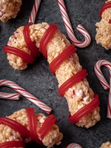 Peppermint candy cane rice krispie treats on a dark gray backdrop with small candy canes around it.