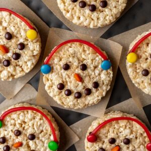 Snowman rice krispie treats decorated with colored candies and a candy string earmuffs.